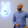 A man standing in front of a neon sign with a peace sign.