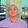 A man in a purple sweater standing next to a dock.
