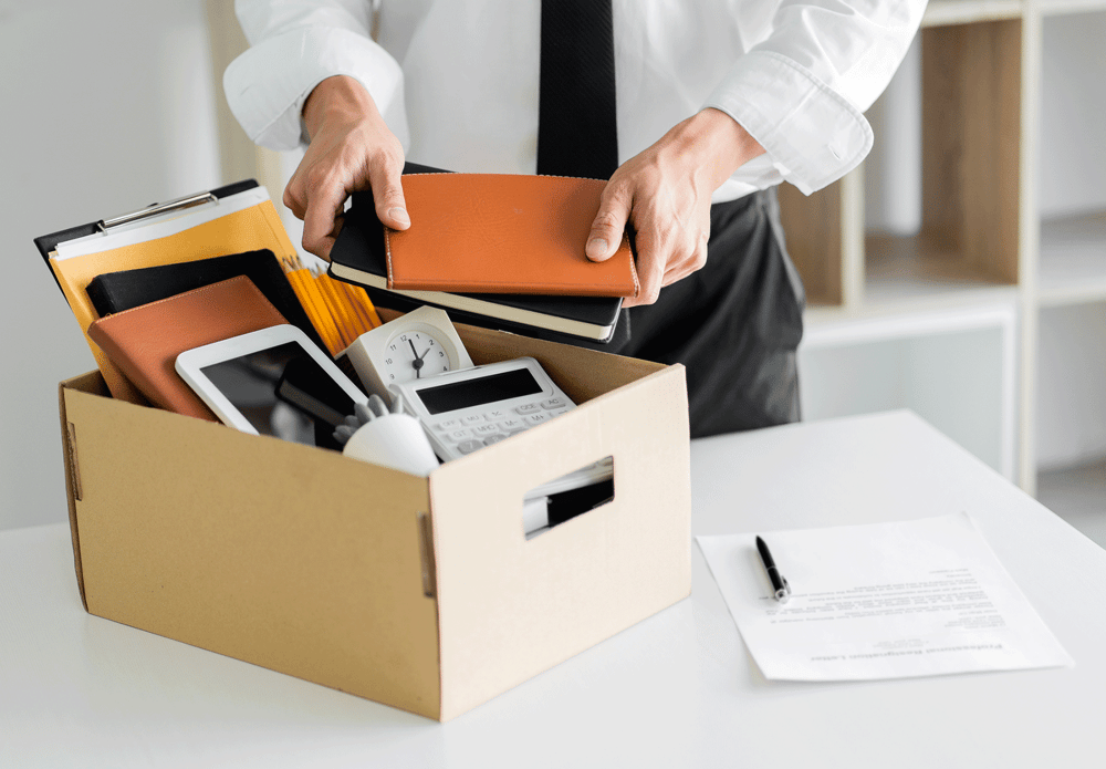 Employee packing personal belongings into a box after job termination in a workplace office.