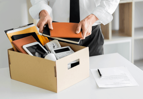 Employee packing personal belongings into a box after job termination in a workplace office.