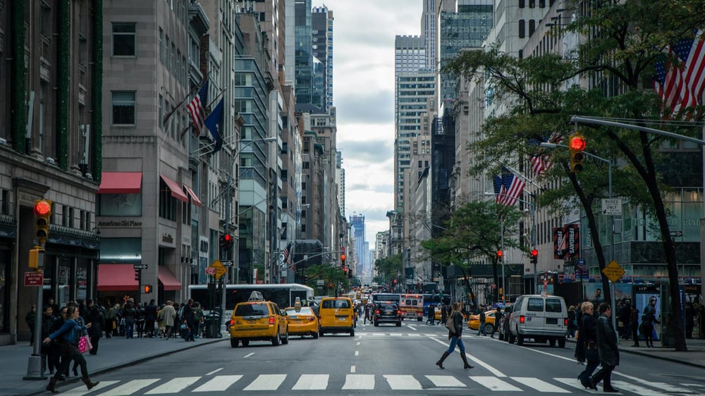 New York City street with yellow taxis, pedestrians crossing, and US flags along buildings, representing US business and payroll environment.