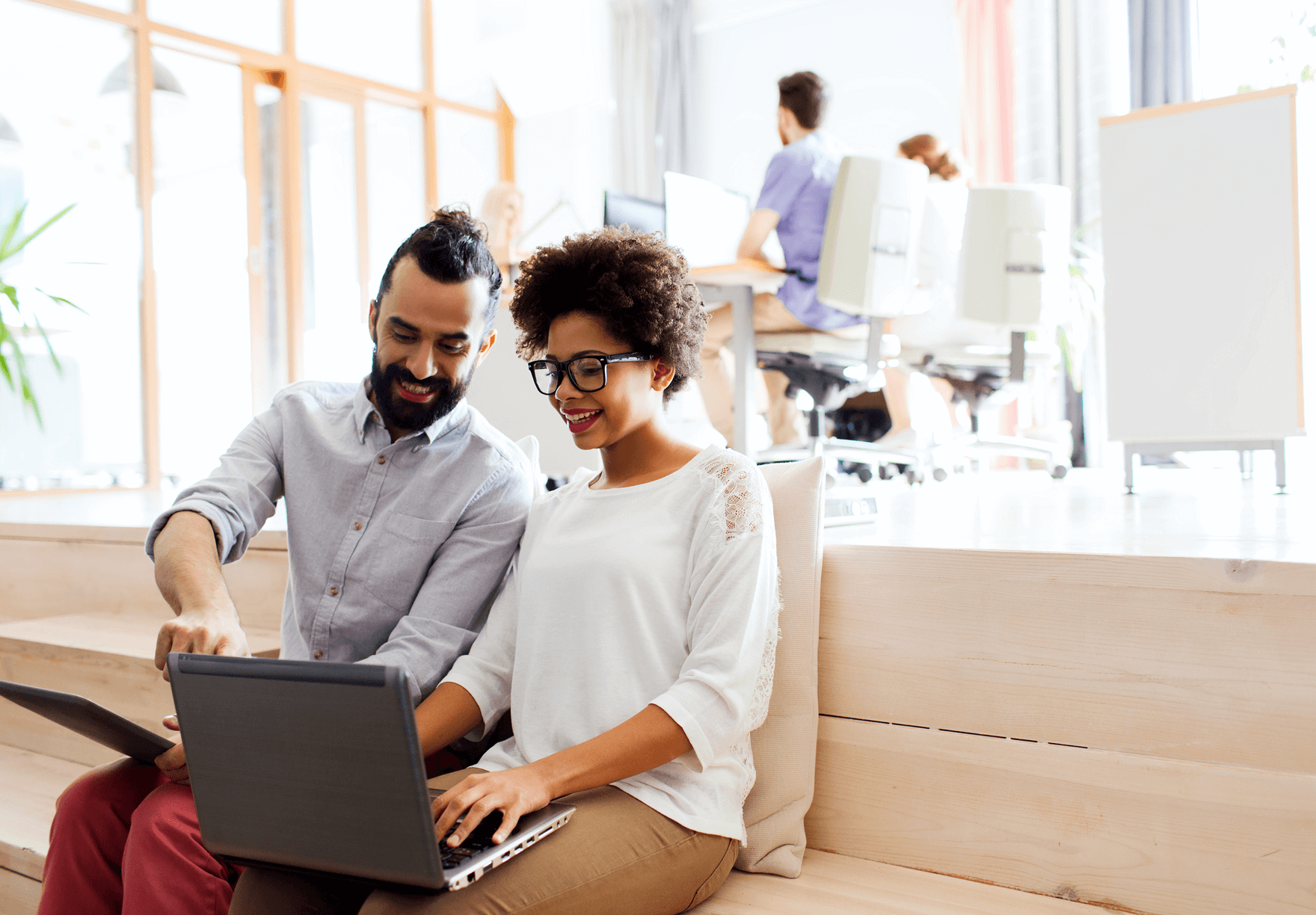 Two smiling hiring managers reviewing work on a laptop in a co-working office space.