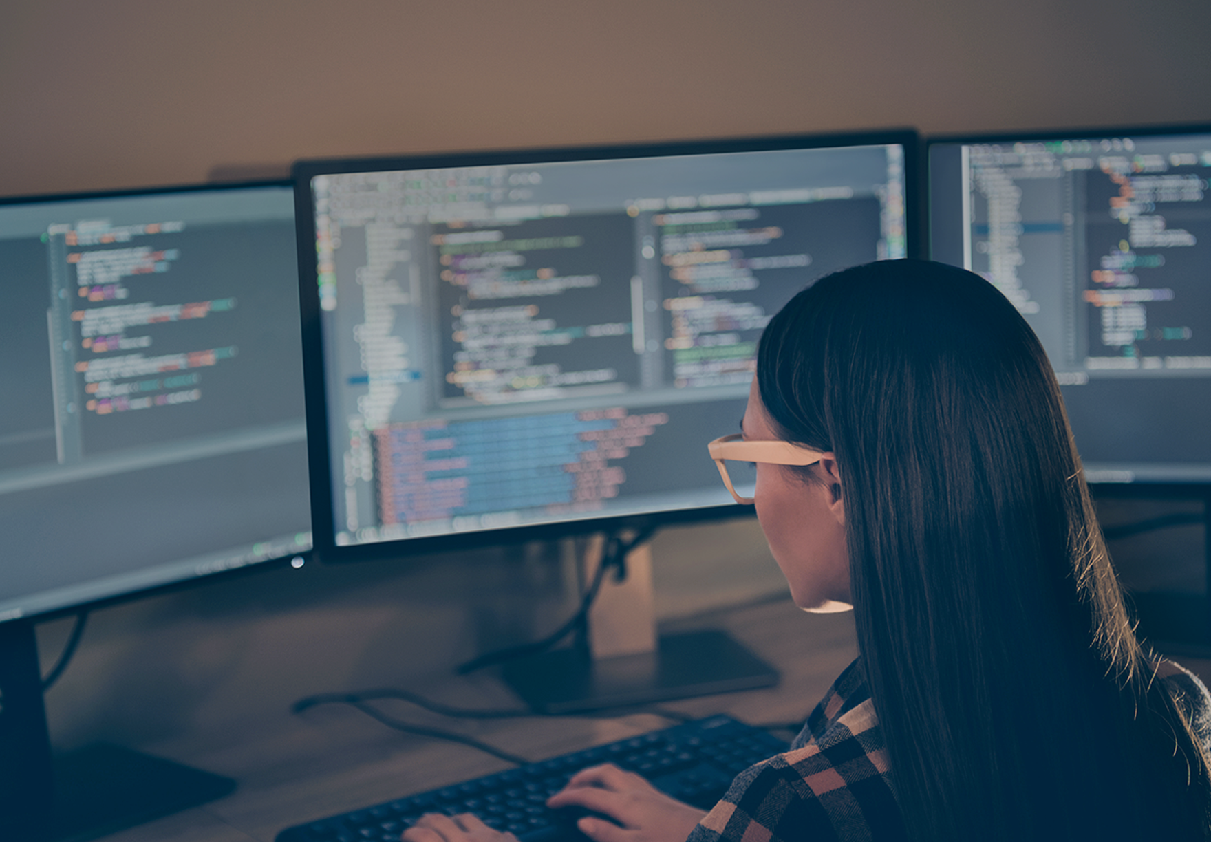 A female remote worker editing form code across multiple desktop monitors
