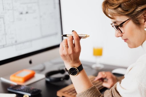 A woman holding a pen sits deep in thought at her desk