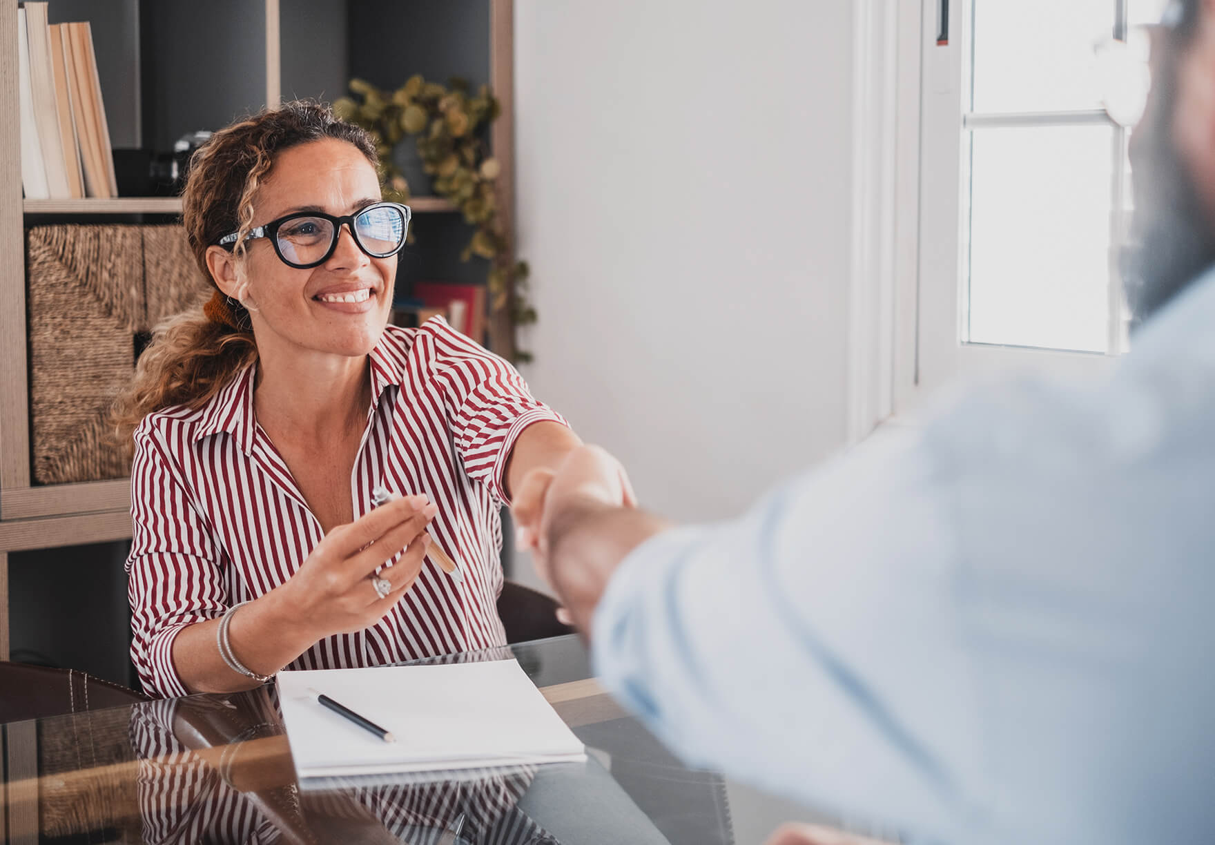 A woman smiling as she shakes the hand of a person across the table
