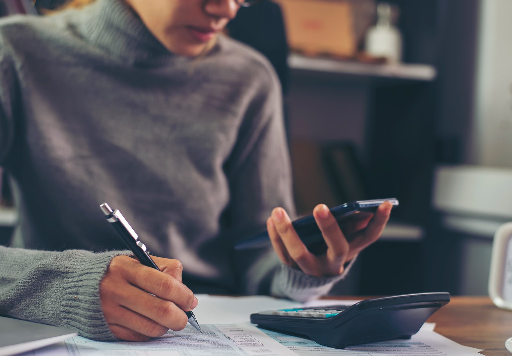 person looking at a phone and calculator while writing